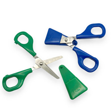 Green and blue Child Self-Opening Scissors, both open with blade guards placed beside them, designed for children with special needs.