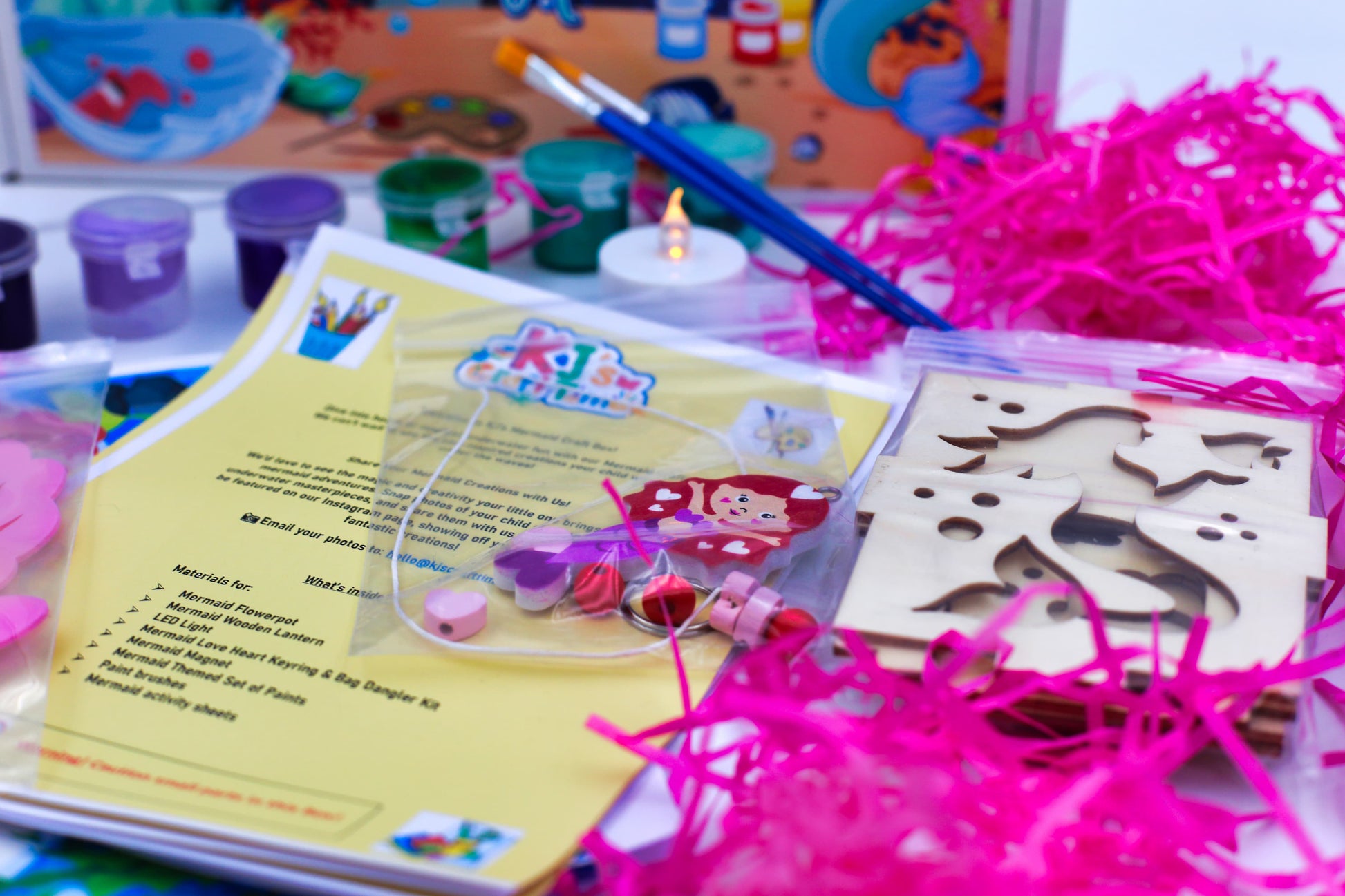 Close-up of mermaid craft kit contents including wooden lantern pieces, beads, mermaid keyring craft, magnet craft and themed activity sheets.
