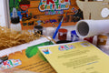 Close-up of pirate craft kit materials including paints, paintbrush, PVA glue, telescope craft and pirate-themed activity sheets.